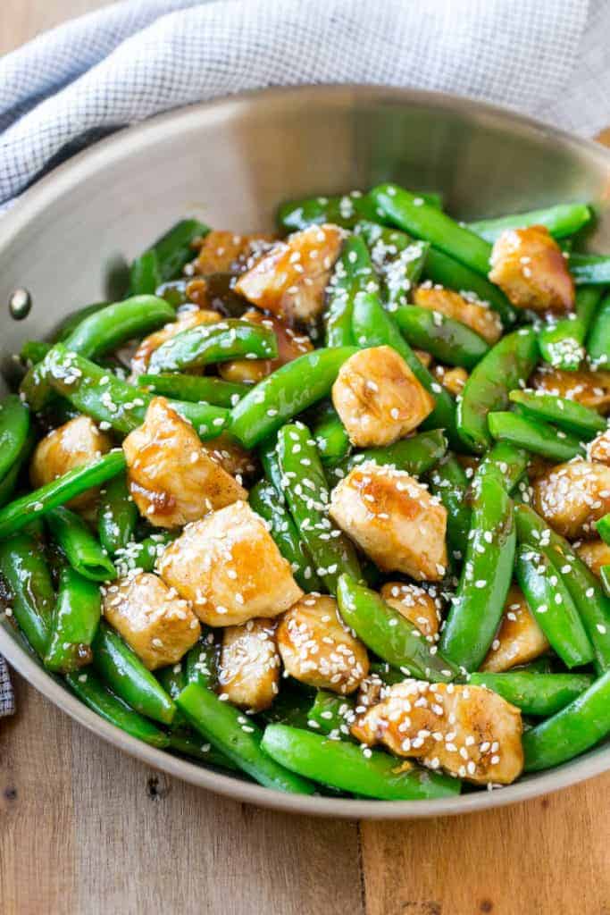 honey chicken bites cooked with sugar snap peas topped with sesame seeds on a pan