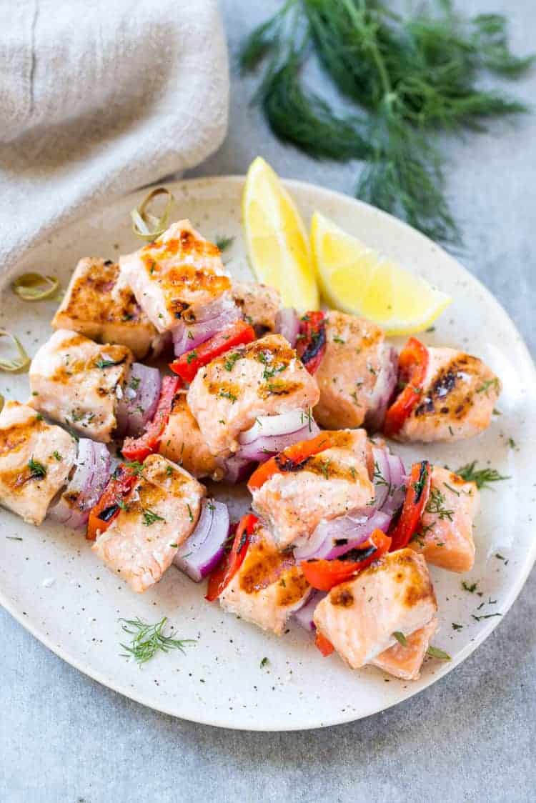 Salmon Skewers on a white plate with lemon and veggies