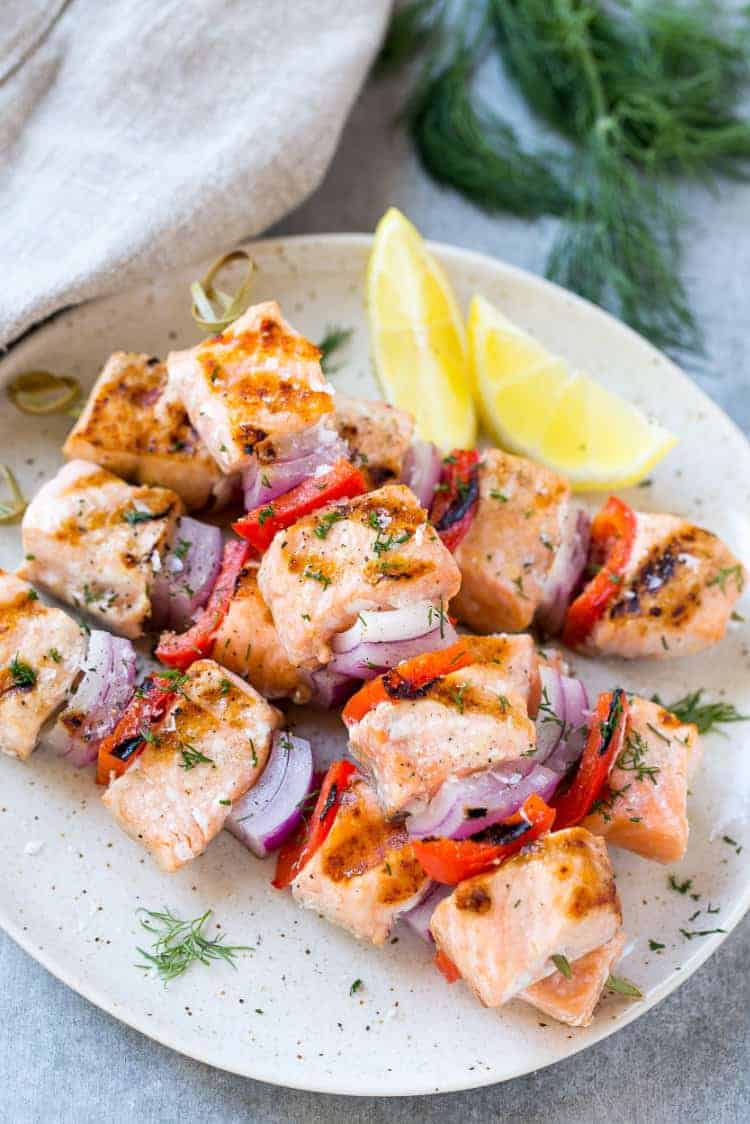 close up of grilled salmon on plate and veggies on skewers 