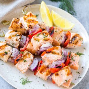 Lemon Dill Salmon Skewers on white plate with lemon and vegetables