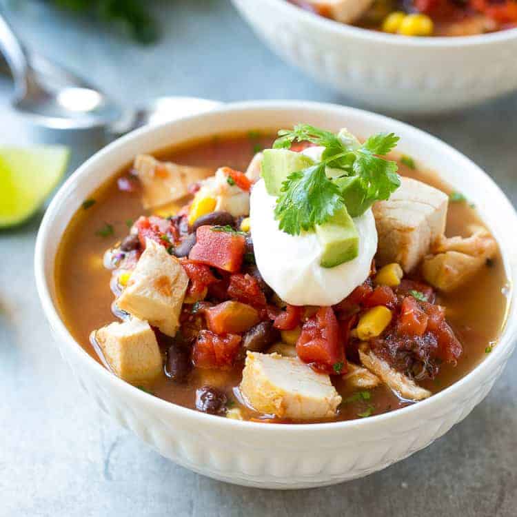 close up white bowl of Mexican chicken soup topped with a small amount of sour cream and fresh cilantrp