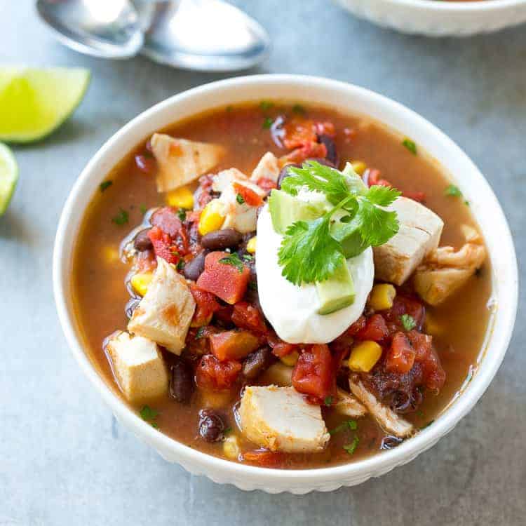 top view of a white round bowl of Mexican chicken soup topped with sour cream