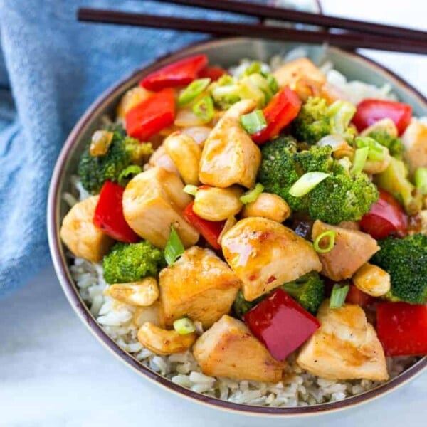 a bowl of rice topped with chicken stir fry and chopsticks over bowl.