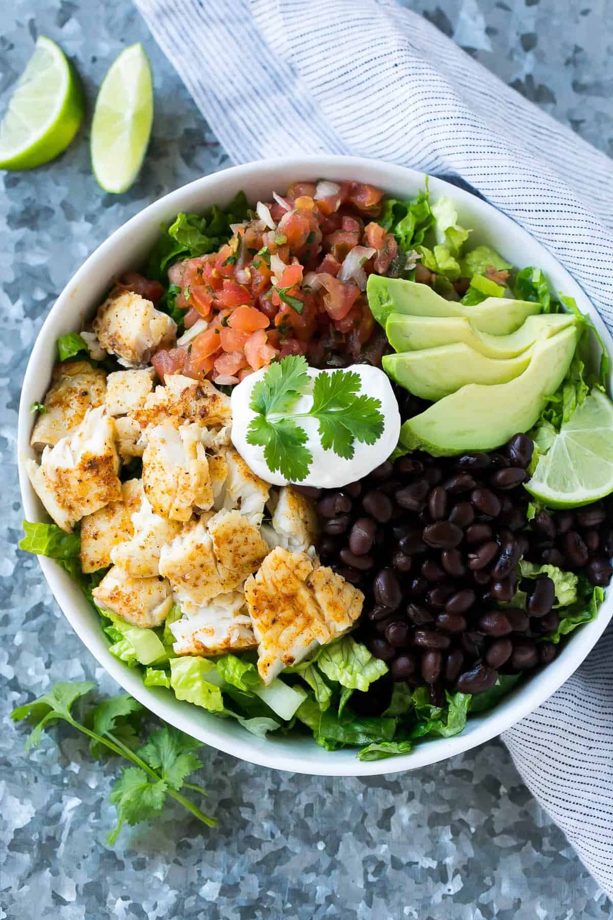 top view of taco salad with fish in bowl with black beans, avocado, sour cream, cilantro, lime, salsa