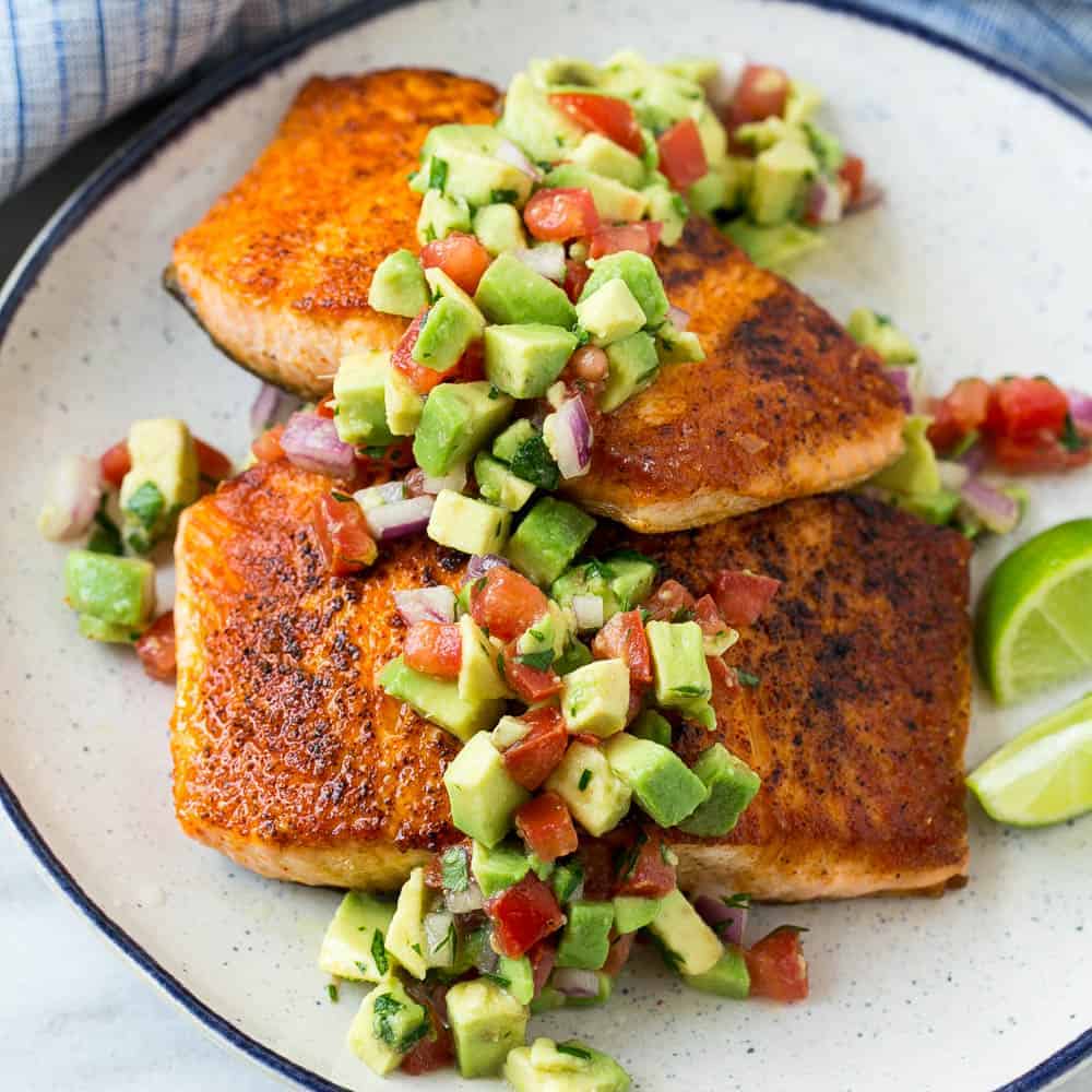 pan seared salmon on white plate with lime and avocado salsa with tomato