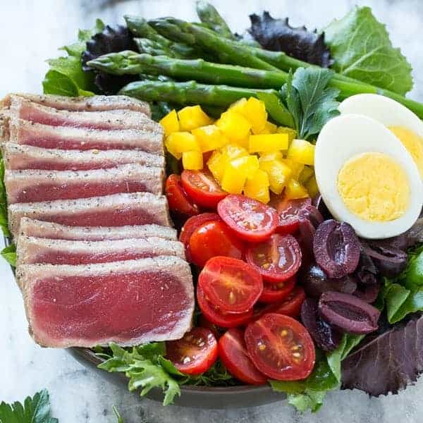 Tuna Nicoise Salad  in a sound bowl with tuna, boiled egg, olives, chopped tomatoes and greens.