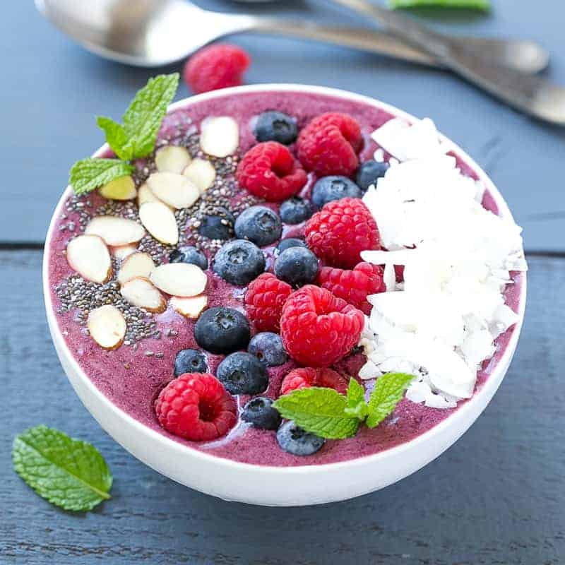 a bowl with berry smoothies topped with fresh berries, sliced almonds, and coconut flakes