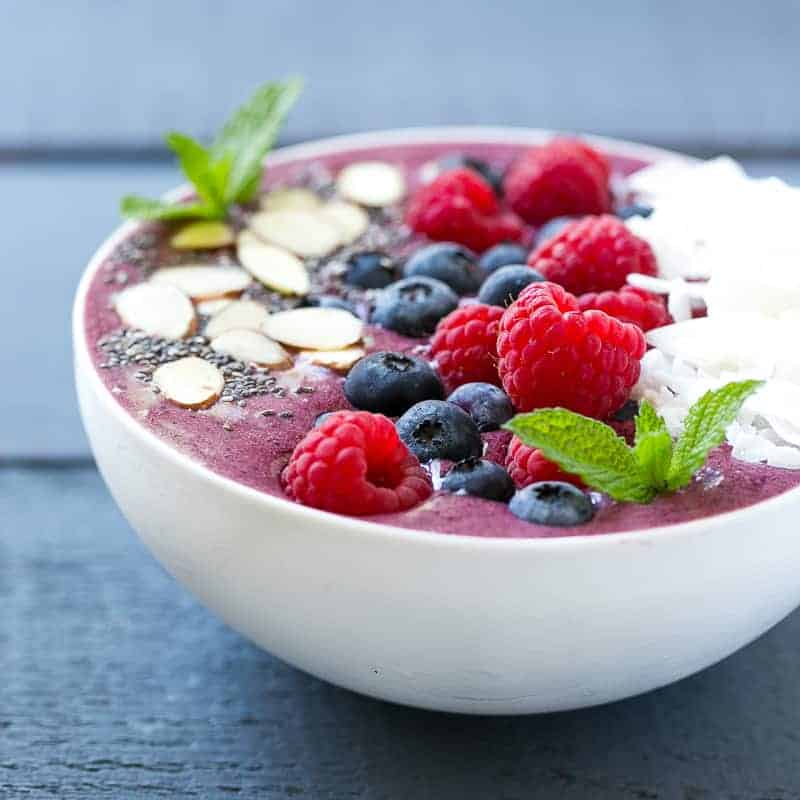 side shot of a bowl of berry smoothies topped with fresh berries and sliced coconut flakes