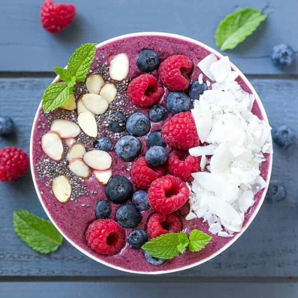 top view of a white round bowl with berry coconut smoothie topped with fresh berries, sliced almonds, and shaved coconut