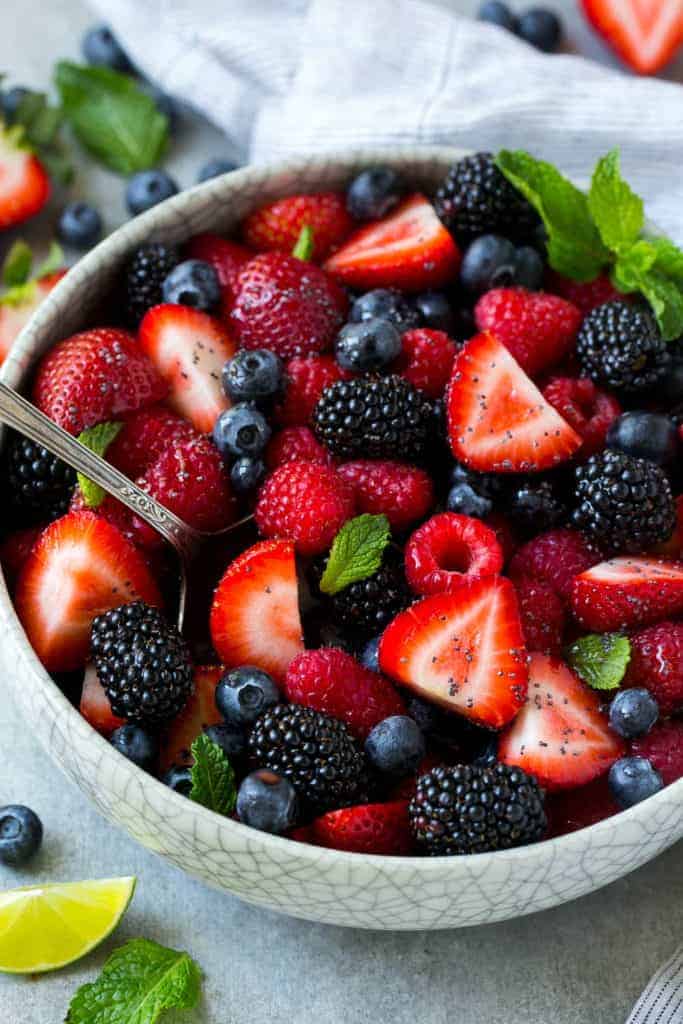 top view of berry fruit salad in a round white bowl with mint and lime wedge garnish