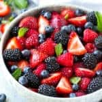 side shot of a white bowl with berries fruit salad topped with fresh mint leaves