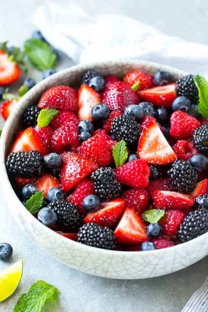 side shot of a white bowl with berries fruit salad topped with fresh mint leaves 