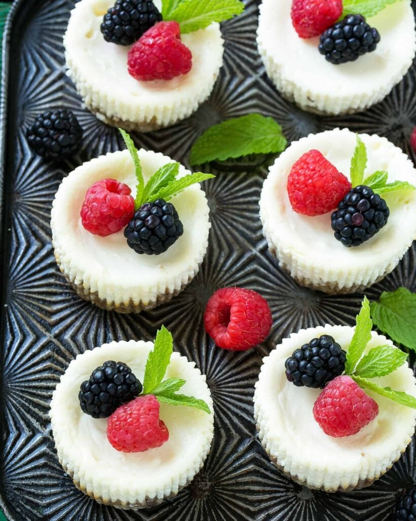 top view of 6 healthy cheesecake bites  lined up on a sheet pan topped with berries 