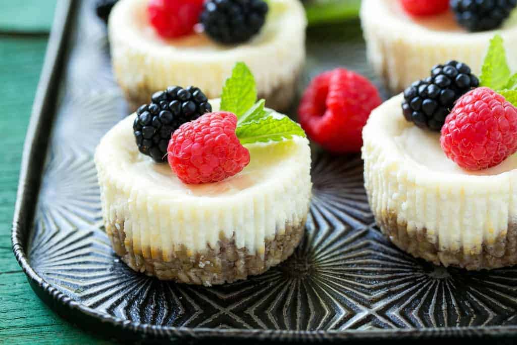 side shot of cheese cake mini bites on a sheet pan topped with berries 