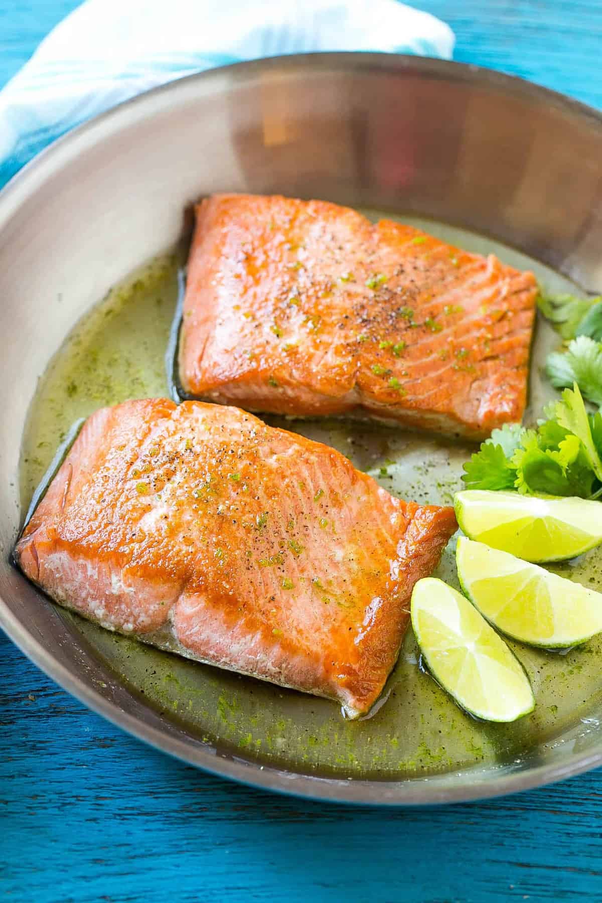 Two glazed salmon fillets in a pan with lime wedges and cilantro