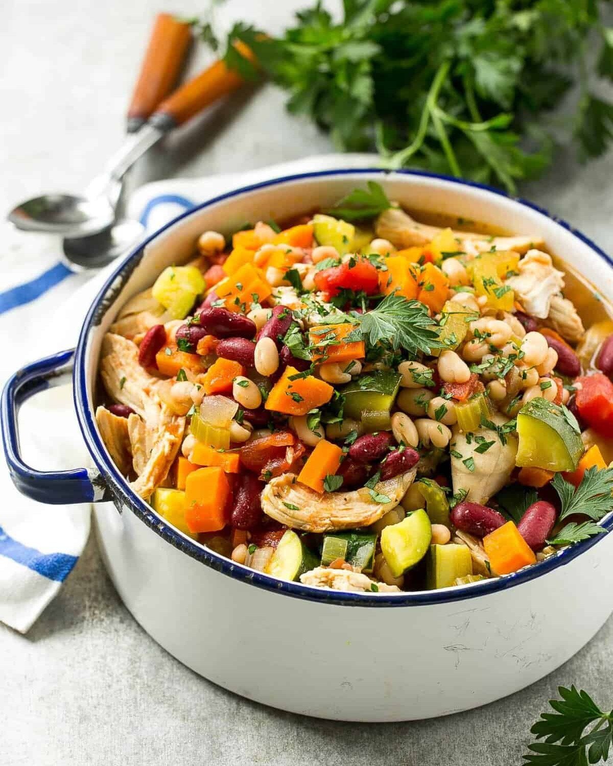 a white pot with chicken and bean soup with veggies.