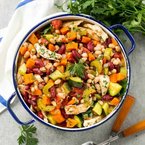 a blue and white pot filled with chicken, bean, and veggies soup.