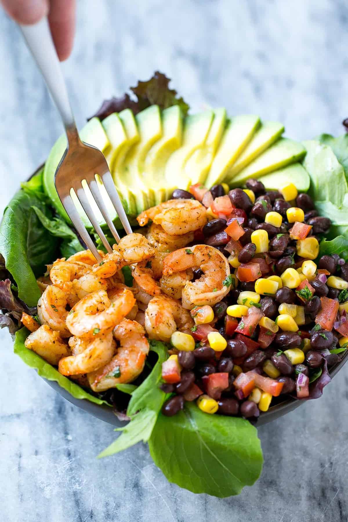 fork reaching into salad bowl with shrimps salsa and avocado