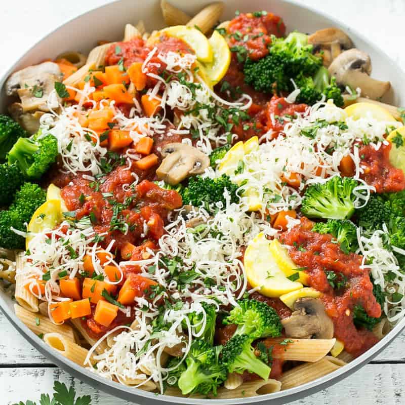 top view of penne pasta primavera in a bowl topped with broccoli mushroom zucchini and shredded parmesan cheese