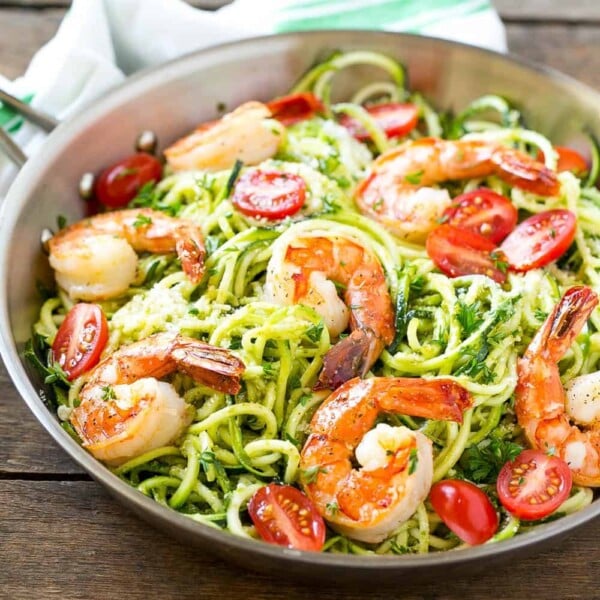 green-looking pesto zoodles topped with cooked shrimp and sliced tomatoes on a pan.