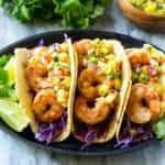 three shrimp tacos on plate with lime and cabbage