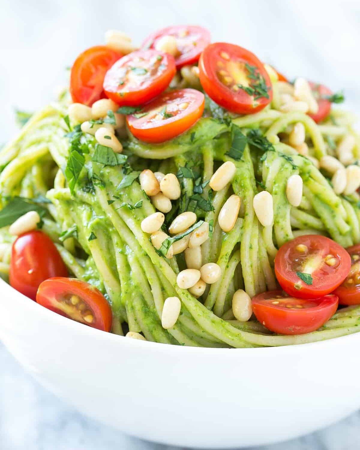 green-looking spaghetti in a round white dish with chopped tomatoes.