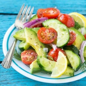 Avocado Cucumber Tomato Salad on a round plate and a fork on the left of the plate