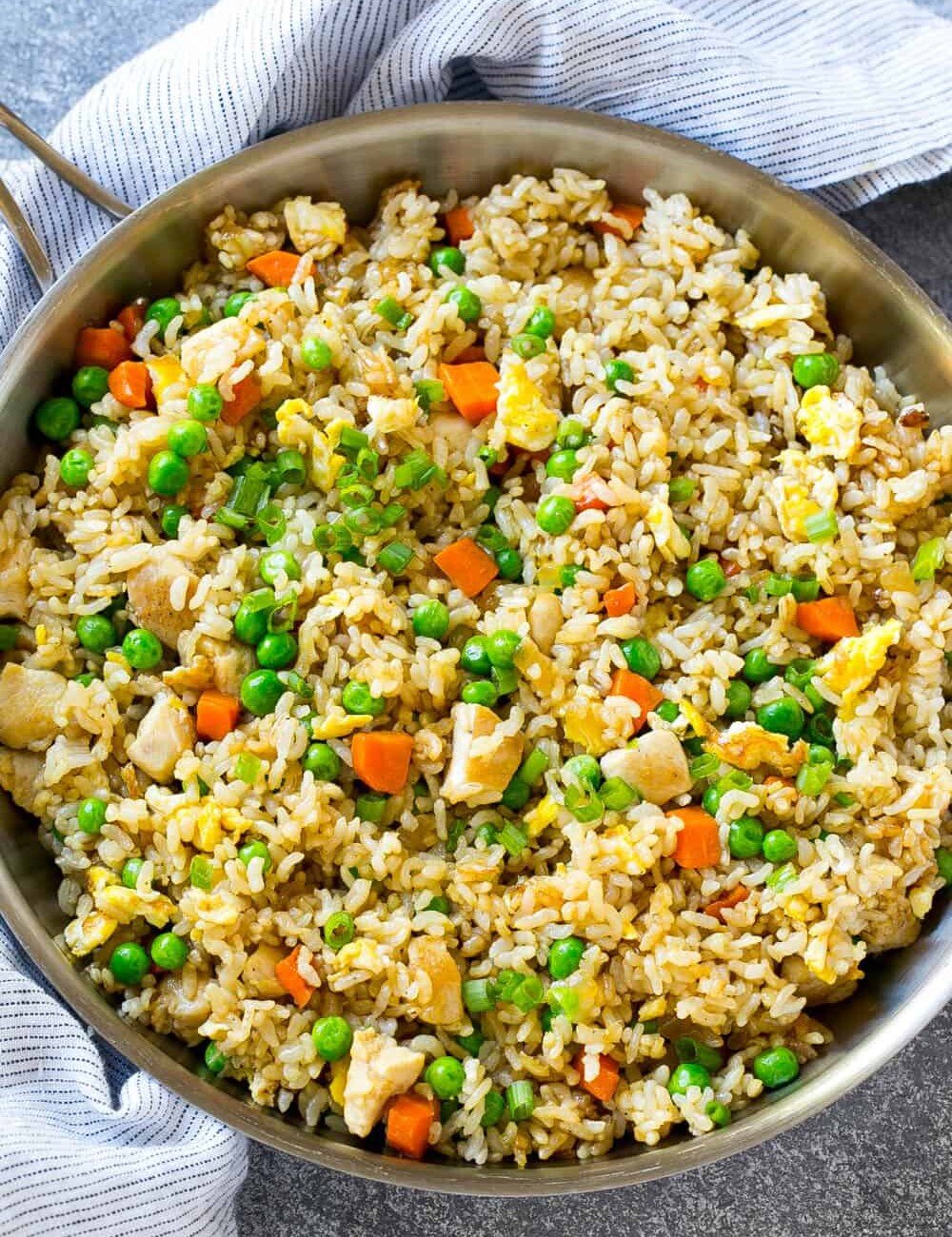 a round skillet with chicken fried rice and veggies.