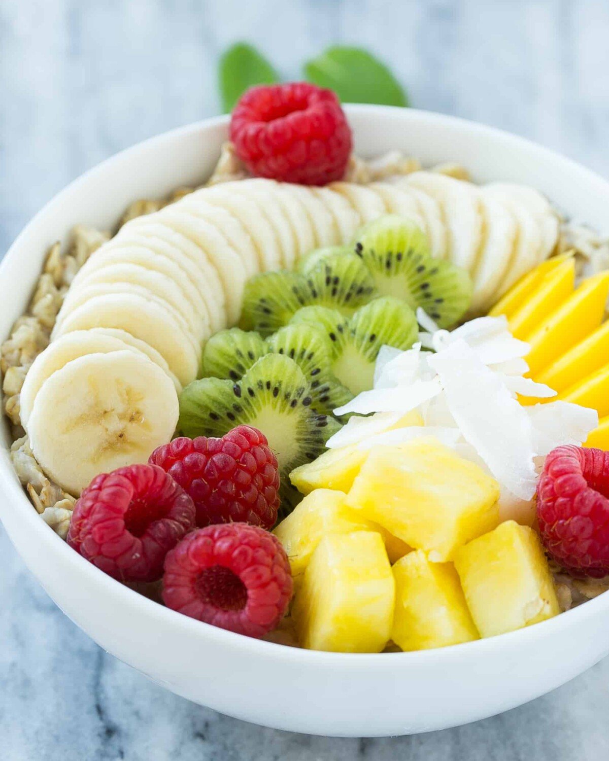 a white bowl of oatmeal topped with a variety of sliced fruits.