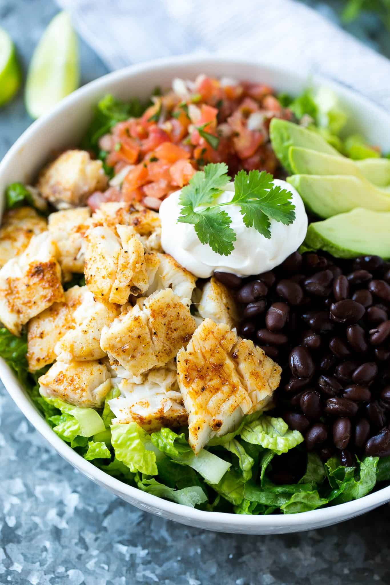 taco salad with fish in bowl with sour cream, cilantro, black beans, salsa, avocado