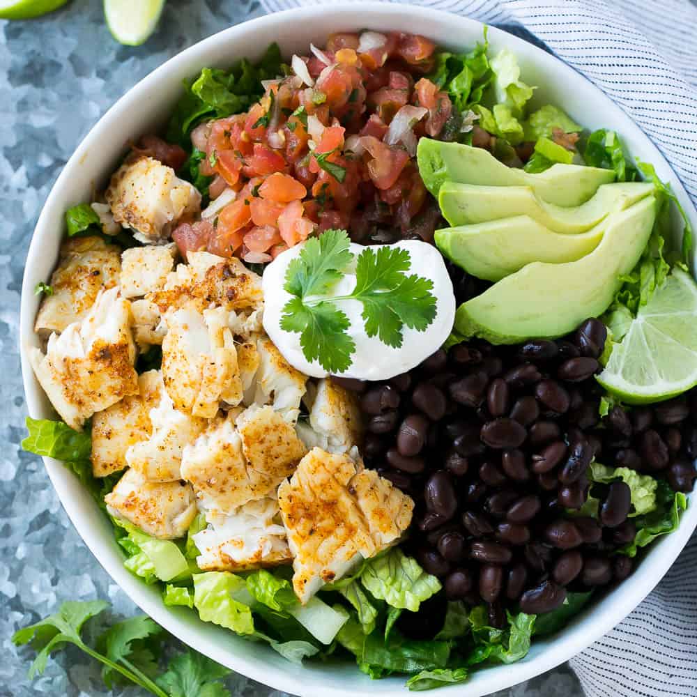 easy fish taco recipe in white bowl with cilantro, black beans, salsa, sour cream, lime