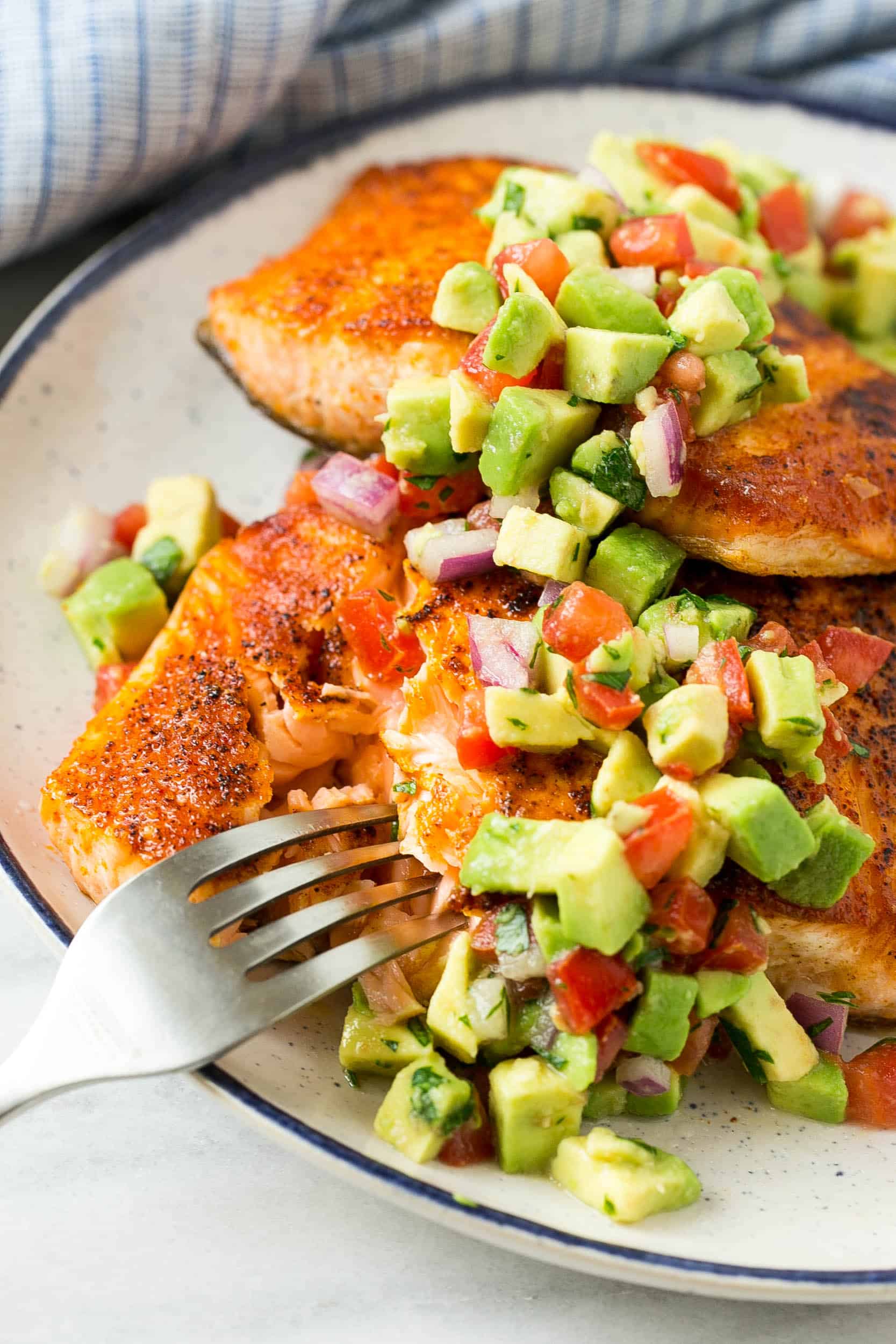 fried salmon on white plate with fork and avocado salsa
