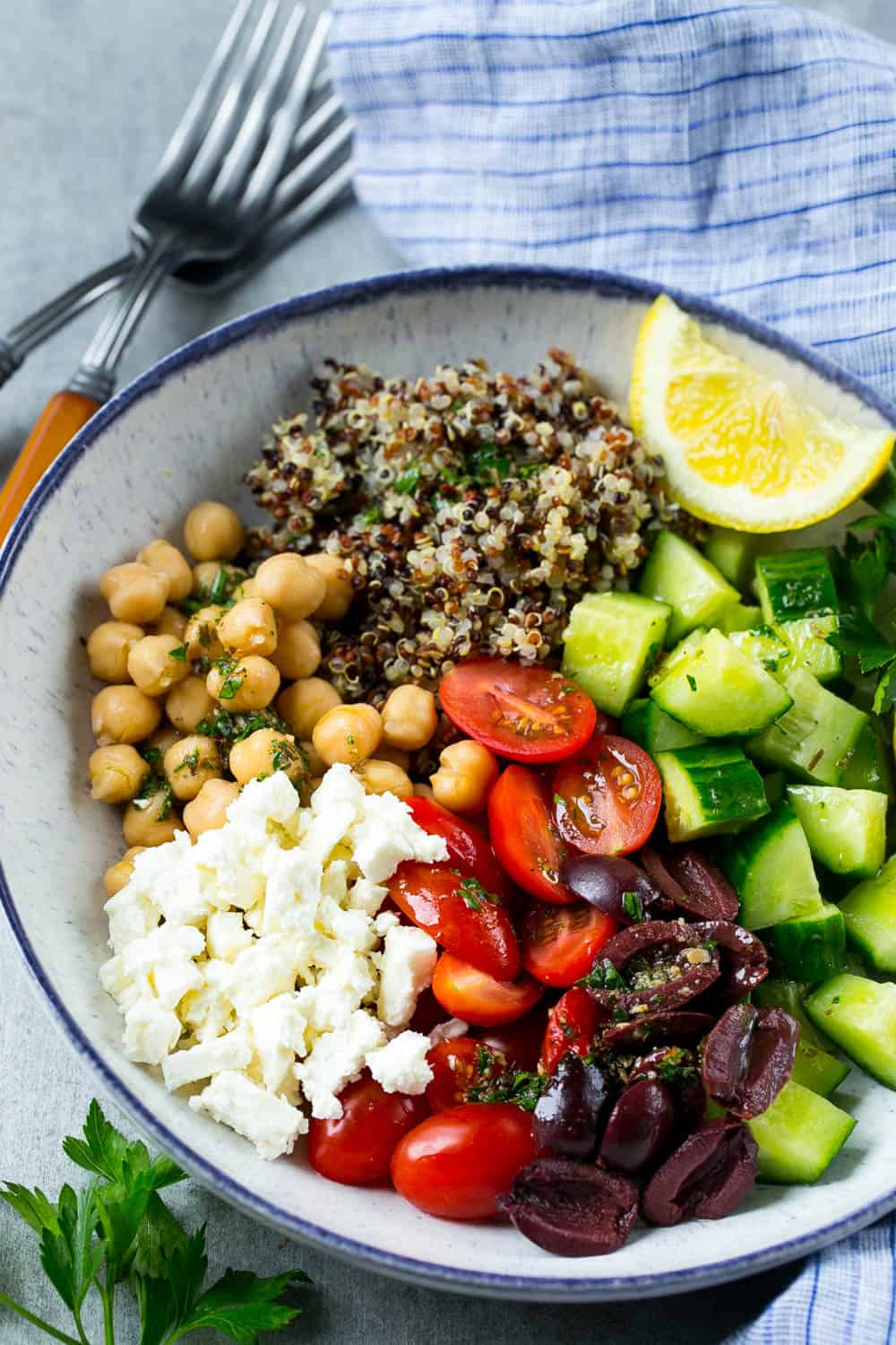 greek quinoa salad in bowl with cucumbers, tomatoes, chickpeas, feta, cooked quinoa, and lemon 