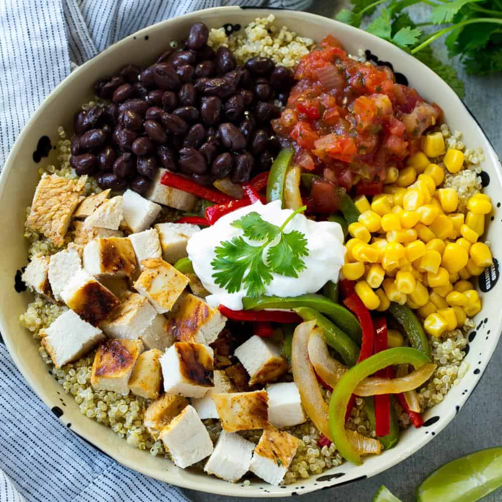 top view of a round bowl with a bed of cooked quinoa, topped with chopped grilled chicken, black beans, corn, salsa, and sauteed onion and green peppers