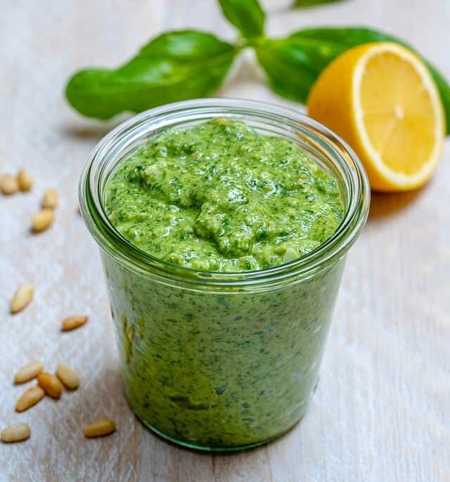 green pesto sauce in a jar with pine nuts and half lemon next to the jar