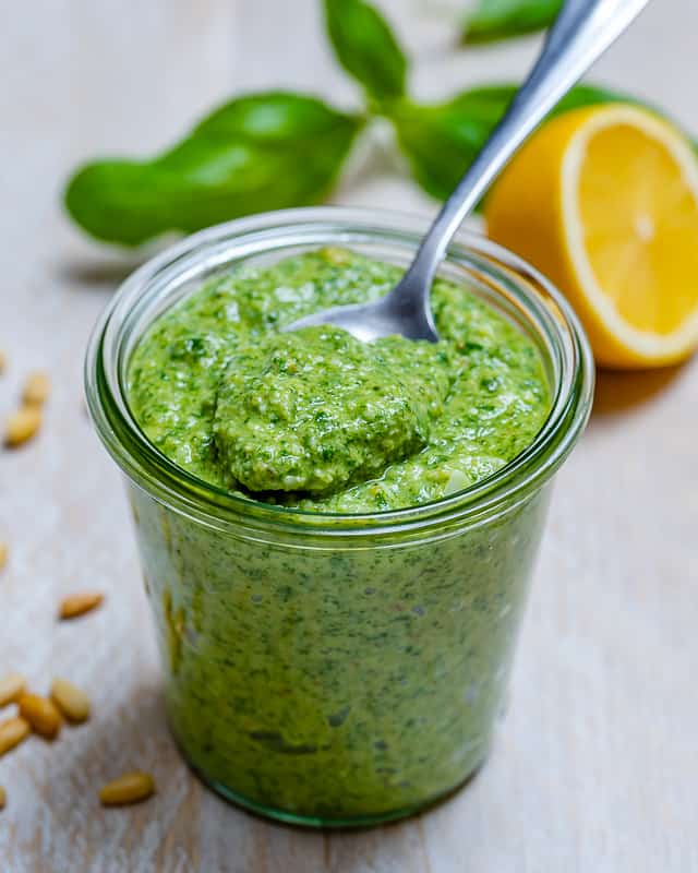 side shot of homemade pesto in a jar with a spoon full of pesto 