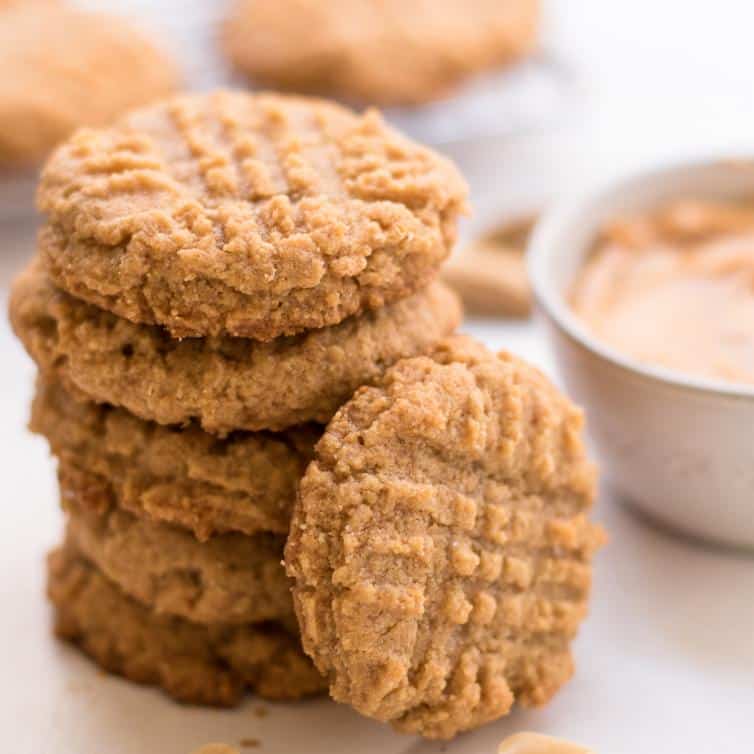 side shot of keto peanut butter cookies stacked over each other next to a small bowl of peanut butter