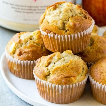 apple muffins stacked on a round white plate in front of a tub of protein powder