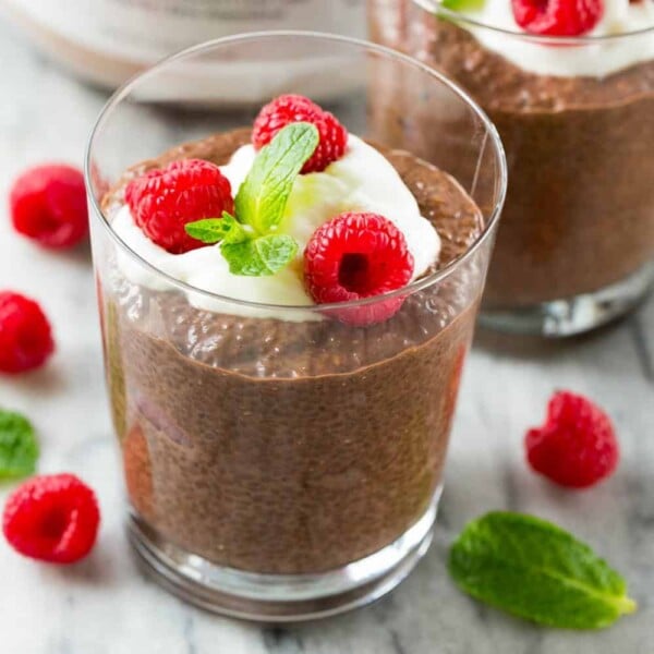 Chocolate Chia Protein Pudding in a glass cup topped with a small portion of yogurt, 3 fresh raspberries, and a small mint leaf.