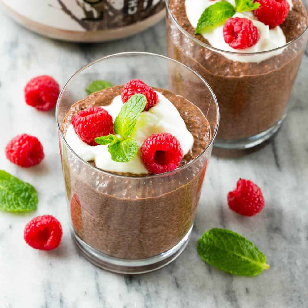 Chocolate Chia Protein Pudding in a glass cup topped with a small portion of yogurt, 3 fresh raspberries, and a small mint leaf.