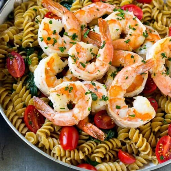 cooked rotini pasta in a skillet topped with cooked shrimp and sliced tomatoes.