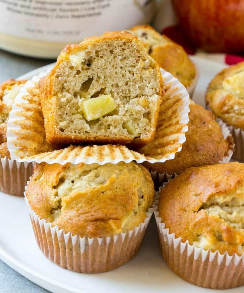 apple muffins on a white plate with one muffins sliced in the middle sitting on top
