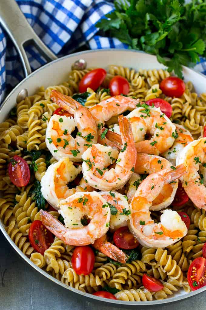 shrimp and rotini pasta in a skillet topped with cherry tomatoes.