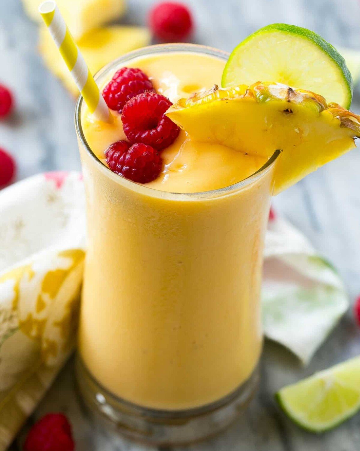 yellow looking smoothie in a cup topped with raspberries.