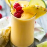 yellow looking smoothie in a cup topped with raspberries.