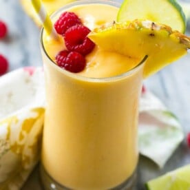 yellow looking smoothie in a cup topped with raspberries.