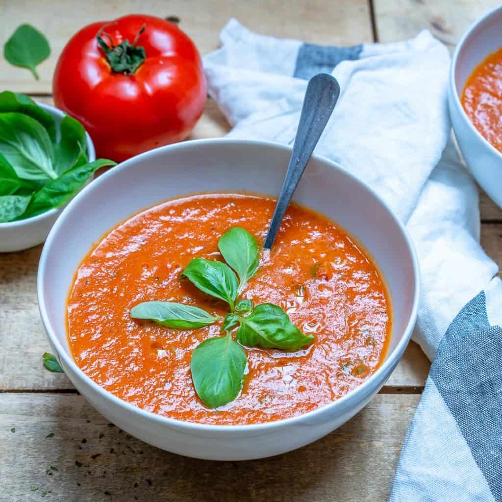 side shot of a bowl of tomato soup topped with fresh basil and a spoon in bowl