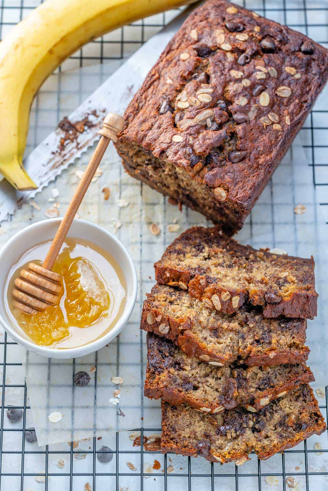 sliced Chocolate Chip Banana Bread on a wire wrack next to bowl of honey.