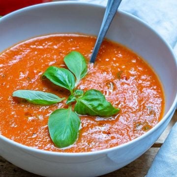 a bowl with red fresh homemade tomato soup with fresh basil and spoon in bowl