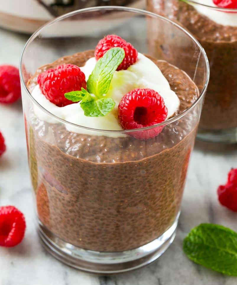 Chocolate Chia Protein Pudding in a glass cup topped with a small portion of yogurt, 3 fresh raspberries, and a small mint leaf.